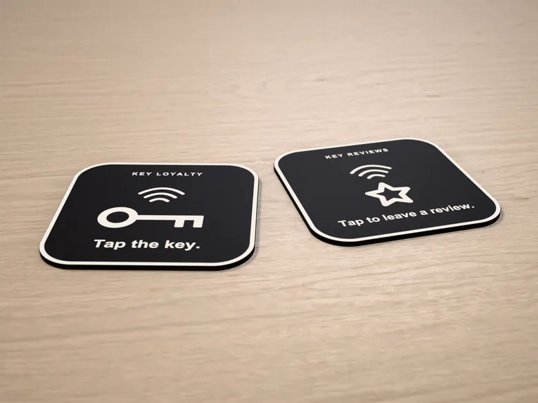 The black KEY Loyalty and KEY Reviews plaques side by side on a light wood counter. Rendered mockup.